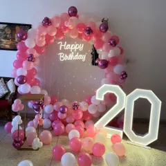 A pretty-in-pink theme for a 20th birthday. This setup includes a full ring of pink and white balloons, fairy lights, and large marquee numbers.