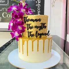 A legendary cake for a legendary man. This two-tiered creation has a gold drip effect on the bottom layer and a solid gold top layer, adorned with fresh purple orchids and a "The Man The Myth The Legend" topper.