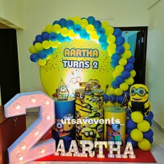 Everyone loves Minions! This fun setup for a second birthday includes a custom Minion-themed backdrop, character-printed plinths for the cake, a large light-up number '2', and of course, a blue and yellow balloon arch.