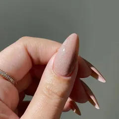 A close-up detail of the shimmering nude polish on a long stiletto nail, showing the fine, reflective glitter within the gel.