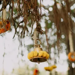 Attention to detail is key. Here, a traditional brass temple bell is adorned with fresh marigolds, hanging from the natural roots of a banyan tree to create a rustic and sacred ambiance.