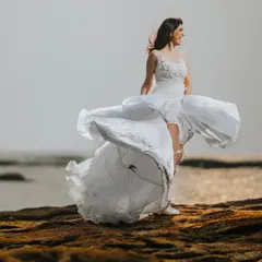 A bridal portrait full of movement and life. The bride's dress is caught by the sea breeze, creating a dynamic and free-spirited image against the ocean backdrop.