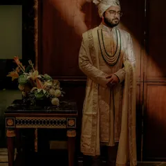 A full length portrait of the groom in his elegant cream sherwani and turban. The dramatic lighting creates a regal and timeless image.