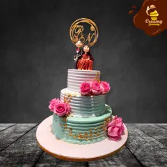 A classic three-tier wedding cake featuring a custom couple topper and delicate pink roses. The combination of textured buttercream and gold leaf accents adds a touch of modern elegance to this celebratory cake.