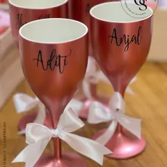 A set of custom-named wine glasses in a beautiful rose gold finish. Each glass is personalized with a bridesmaid's name and tied with a delicate white ribbon, making it a perfect keepsake.