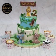 A delightful two-tier jungle safari cake with matching animal-themed cupcakes. This choco-chip cake is adorned with a fondant lion, monkey, elephant, and bear.