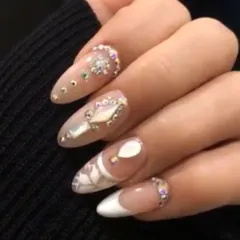 A close-up of intricate bridal nail art. This design features delicate white patterns, shimmering gems, and 3D elements on a soft, natural base, perfect for the bride who wants a detailed and luxurious look.