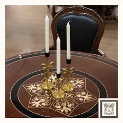 These exquisite gold-finished metal candle stands, with their delicate bow details, sit atop a dining table with a beautiful floral inlay. They are perfect for adding a warm glow to a vintage or regal interior.