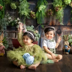 Double the fun, double the cuteness! This shot captures the sweet interaction between two babies during a shared studio session with a rustic green theme.
