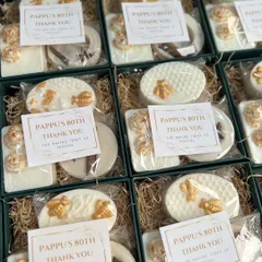 A vintage-themed return favor for an 80th birthday celebration. These elegant white and gold boxes include two custom soaps and a cinnamon wardrobe freshener, with personalized thank you tags.