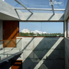 A glass skylight floods the central atrium of the apartment building with natural light, which cascades down the exposed concrete walls, creating dramatic shadows and illuminating the common areas.
