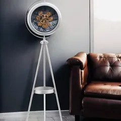 A luxury tripod standing clock crafted from high-quality steel with a silver metallic finish. The exposed moving gears and functional lower shelf make it a timeless piece of decor.