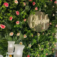 A beautiful and simple selfie point featuring a "Better Together" neon sign on a lush green wall dotted with pink roses.