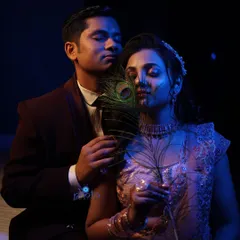 A creative and moody engagement portrait using a peacock feather and colored lighting. This type of artistic shot adds a unique and memorable element to the event album.