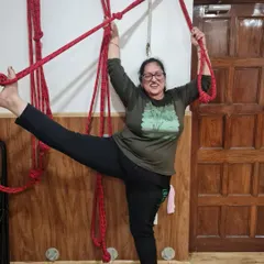 The joy of practice is evident on this student's face as she uses the ropes for a supported standing split. The ropes provide security, allowing her to explore her flexibility with a sense of playfulness.