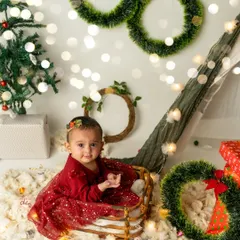 Sitting pretty in her Christmas sleigh. This baby girl is ready for the holidays in a setup complete with wreaths, presents, and a decorated tree.