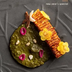 A modern interpretation of a winter classic, paneer with tadka saag. The paneer is scored and grilled, served alongside a creamy spinach puree and garnished with delicate edible flowers.