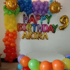 A vibrant rainbow-themed decoration for a 9th birthday. This setup includes a colorful balloon column, rainbow "Happy Birthday" foil letters, and fun smiling sun foil balloons.