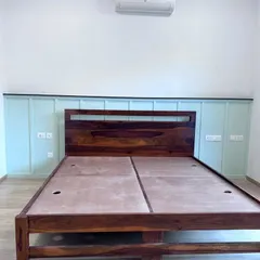 The solid wood frame of a bed, ready for the mattress. The image shows the quality of the wood and the panelled headboard design against a soft green wall.