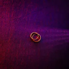 An artistic photo of two wedding bands intertwined on a textured, colorful surface. The lighting creates a moody and romantic feel.