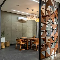 A modern dining area featuring a unique geometric partition wall. The combination of concrete-finish walls, a wooden dining set, and artistic pendant lights creates an industrial-chic vibe.