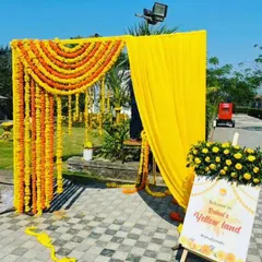 An outdoor Haldi function entrance, which we called "Welcome to Yellow Land." The setup features a simple frame decorated with fresh marigold garlands and a yellow curtain, perfect for a garden or lawn event.