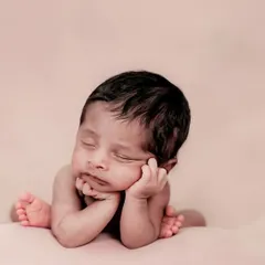 So tiny and new. This classic 'chin on hands' pose is a favorite for newborn photography, highlighting their sweet, sleepy face.