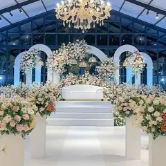 An opulent, all-white stage in a glasshouse, featuring grand arches and an abundance of flowers for a luxurious feel.