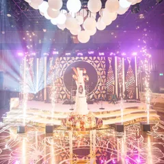 This is the moment. The cake cutting for Shivani and Nikhil, surrounded by our bespoke production. You can see the custom monogrammed dance floor, the multi-level stage, the orb centerpiece lighting, and perfectly timed pyrotechnics. We design every element to build up to these peak moments of celebration.