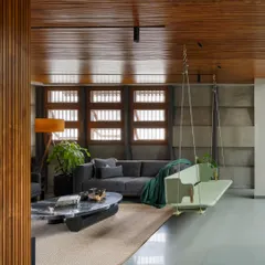 The living area of the 'Heirlooms in Concrete' home, where a contemporary swing adds a playful element. We combined a warm wood ceiling, textured concrete walls, and polished grey flooring to create a space that feels both expansive and intimate.