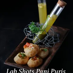 This is how we reimagine a classic. Our 'Lab Shots Pani Puris' combine the tangy, crisp flavors of street-style chaat with a playful, fine-dining presentation, serving the spiced water in elegant test tubes for a memorable bite.