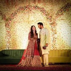 A happy, candid moment between the couple on their reception stage. The stunning wall of flowers creates a perfect backdrop for their joy.