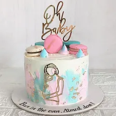 "Bun in the oven, almost done." This watercolor-style baby shower cake with pink and blue splashes is perfect for a gender-neutral celebration. The macarons and "Oh Baby" topper add a touch of fun.