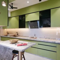 A wide-angle view showcasing the parallel counters of the sage green kitchen. The combination of matte green cabinets, black profile details, and a textured marble countertop creates a balanced and luxurious feel.