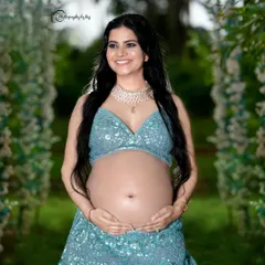 A joyful bare-bump portrait in our outdoor setting. The mother-to-be is wearing a sparkling blue two-piece lehenga, celebrating her pregnancy with confidence and style.