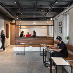 The café and lounge area is designed with warm leather seating and minimalist tables to encourage informal meetings and social connections. The open layout ensures a constant visual link to the rest of the dynamic co-working environment, promoting a sense of community.