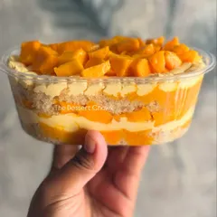 My Fresh Mango Cake Tub held up to show the beautiful layers. It features vanilla sponge, mango mousse, and lots of fresh mango chunks.