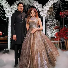 A grand entrance for a grand occasion. The groom wears a classic black sherwani, a timeless choice that exudes elegance and perfectly complements his partner's magnificent metallic gown at their reception.