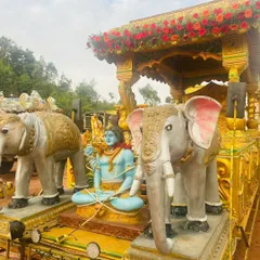 A procession chariot featuring a statue of Lord Shiva, flanked by two decorative elephants and adorned with a floral canopy.