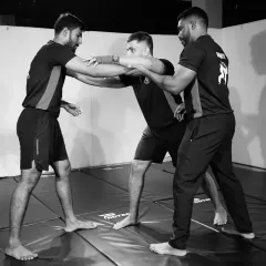 Our coaches provide hands-on instruction for grappling techniques. Here, a coach corrects the posture and grip of two students practicing a takedown entry.
