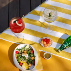 A perfect poolside scene: a healthy salad, two colorful cocktails, and sparkling water on a bright yellow lounger. This is the picture of leisurely indulgence.