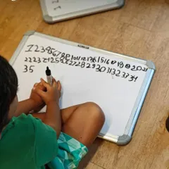 A child practices writing numbers on a whiteboard. We see this not as a test, but as a developmental stage. Reversed numbers and uneven lines are milestones, showing a brain that is learning to coordinate hand, eye, and an understanding of symbols.