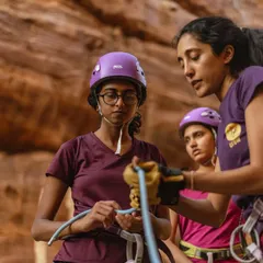 Women learning the ropes from other women. An instructor teaches a participant how to tie a figure-eight knot, a critical safety skill for rope climbing.
