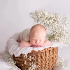 A newborn rests peacefully in a rustic wicker basket, surrounded by ethereal white gypsophila flowers. This portrait combines natural textures with soft lighting to create a timeless and angelic image.
