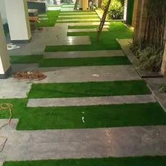 An in-progress shot of a modern walkway installation. I created a pattern by laying strips of artificial grass between large grey stone tiles, resulting in a contemporary and graphic look.