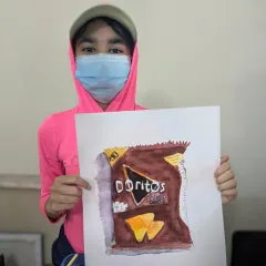 Eleven-year-old Ariya with her impressive watercolor painting of a Doritos bag. This object study exercise teaches students to observe and replicate complex textures, reflections, and typography.