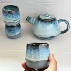 Holding one of the small tea cups from the set. They are designed without handles, in a traditional style, to be warmed by the tea and cupped in your hands.