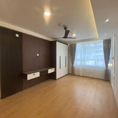 A view of a spacious bedroom featuring a dark wood accent wall with a floating console, complemented by a floor-to-ceiling white wardrobe and soft, natural light from the window.