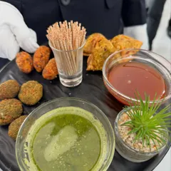 A platter of assorted fried appetizers served with green and sweet chutneys. This selection includes mini samosas and vegetable cutlets, classic choices for any event.