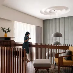 **Amber House, Ahmedabad:** The upper-level passage overlooks the main living area, maintaining a sense of connection between floors. The wooden railings continue the theme of vertical lines, creating visual rhythm and a feeling of warmth and craftsmanship.